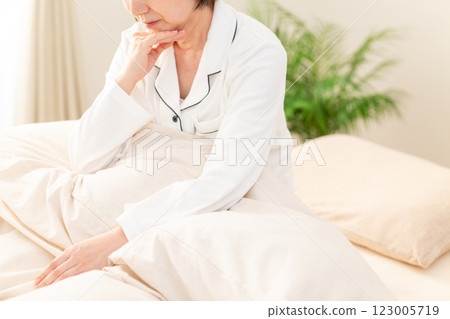 一名身穿白色睡衣的中年婦女早上在臥室裡憂心忡忡 一名身穿白色睡衣的中年婦女早上在臥室裡憂心忡忡 123005719