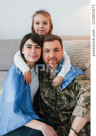 Ukrainian flag is on the shoulders. Soldier in uniform is at home with his wife and daughter 123005871
