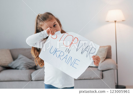 Little girl standing at home and holding banner with stop war in Ukraine text 123005961