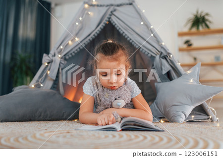Reading the book. Cute little girl playing in the tent that is in the domestic room Reading the book. Cute little girl playing in the tent that is in the domestic room 123006151