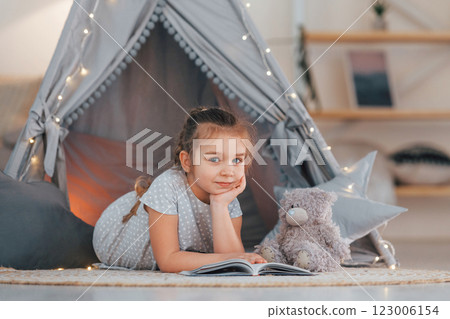 Laying down on the ground. Cute little girl playing in the tent that is in the domestic room Laying down on the ground. Cute little girl playing in the tent that is in the domestic room 123006154