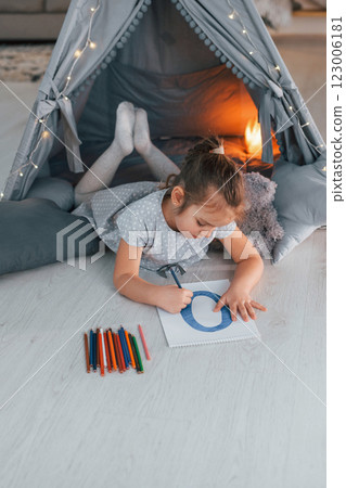 Writing letter. Cute little girl playing in the tent that is in the domestic room Writing letter. Cute little girl playing in the tent that is in the domestic room 123006181