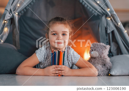With writing equipment. Cute little girl playing in the tent that is in the domestic room 123006190