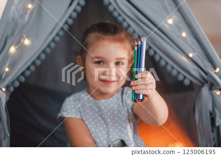 Holding pencils. Cute little girl playing in the tent that is in the domestic room 123006195