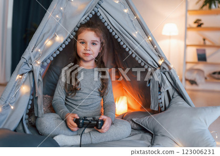 Playing videogame. Cute little girl playing in the tent that is in the domestic room Playing videogame. Cute little girl playing in the tent that is in the domestic room 123006231