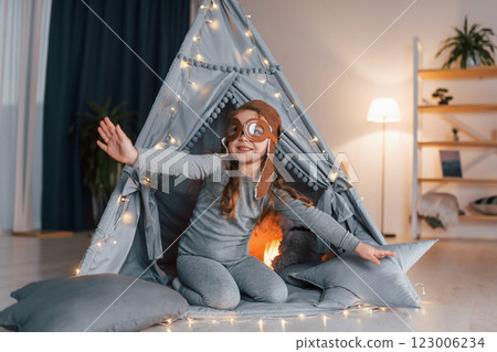 In pilot glasses. Cute little girl playing in the tent that is in the domestic room 123006234