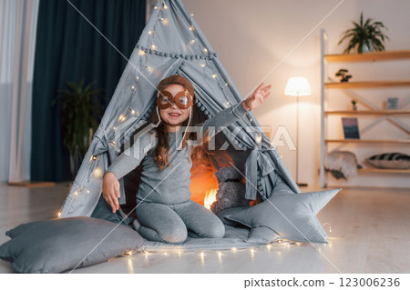 In pilot glasses. Cute little girl playing in the tent that is in the domestic room In pilot glasses. Cute little girl playing in the tent that is in the domestic room 123006236