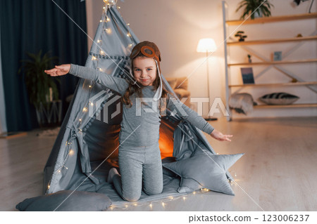 In pilot glasses. Cute little girl playing in the tent that is in the domestic room In pilot glasses. Cute little girl playing in the tent that is in the domestic room 123006237