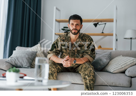 On the sofa. Post traumatic stress disorder. Soldier in uniform sitting indoors 123006353