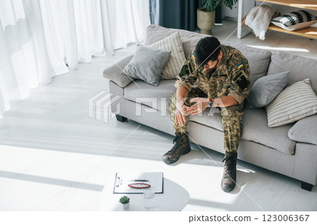 Bad mood. Post traumatic stress disorder. Soldier in uniform sitting indoors 123006367