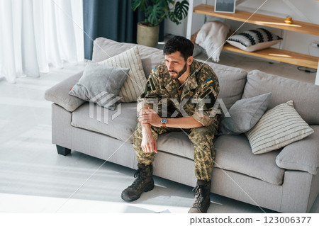 Bad mood. Post traumatic stress disorder. Soldier in uniform sitting indoors 123006377