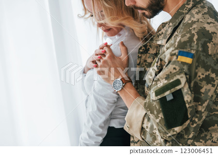 Flag of Ukraine. Soldier with his wife standing indoors and embracing Flag of Ukraine. Soldier with his wife standing indoors and embracing 123006451