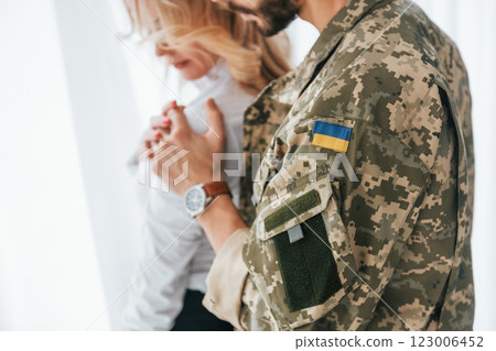 Flag of Ukraine. Soldier with his wife standing indoors and embracing Flag of Ukraine. Soldier with his wife standing indoors and embracing 123006452
