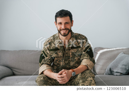 Soldier in uniform is indoors in the domestic room. Sitting on the sofa 123006510