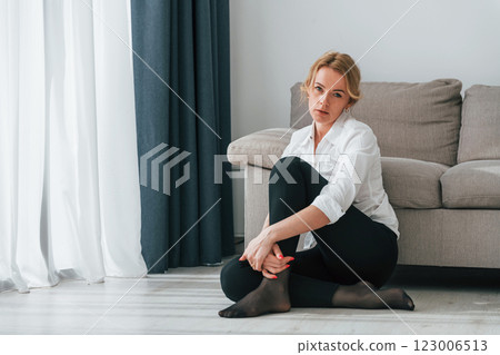 Woman in formal wear sitting on the floor near sofa in domestic room 123006513