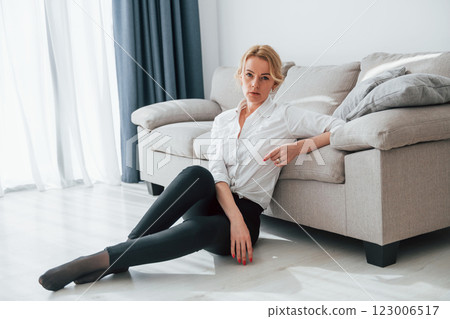 In black jeans. Woman in formal wear sitting on the floor near sofa in domestic room In black jeans. Woman in formal wear sitting on the floor near sofa in domestic room 123006517