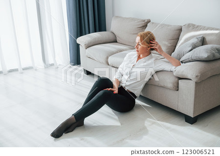 In black jeans. Woman in formal wear sitting on the floor near sofa in domestic room 123006521