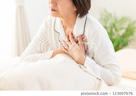 Middle-aged woman in white pajamas suffering from chest pain in her bedroom in the morning 123007676