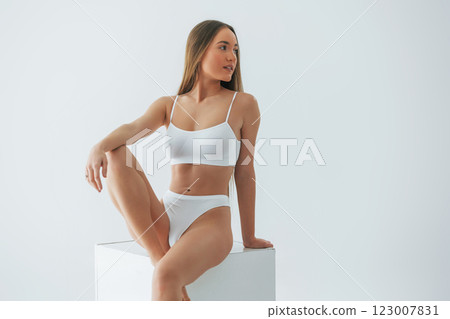 Sitting on white cube. Woman in underwear with slim body type is posing in the studio Sitting on white cube. Woman in underwear with slim body type is posing in the studio 123007831