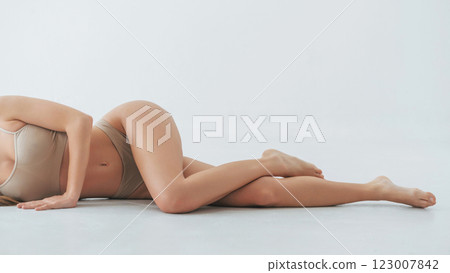 Laying down on the floor. Woman in underwear with slim body type is posing in the studio 123007842