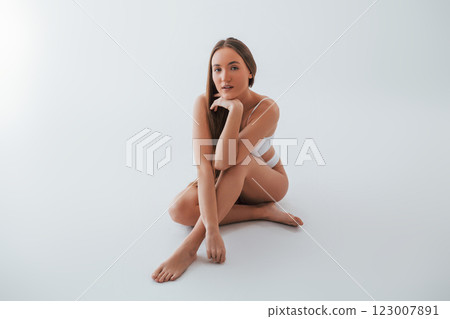 Beautiful model sitting on the floor. Woman in underwear with slim body type is posing in the studio 123007891