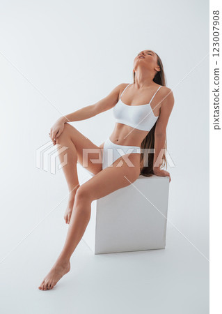 Sitting on white cube. Woman in underwear with slim body type is posing in the studio 123007908