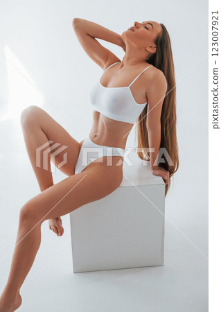 Posing on the white cube. Woman in underwear with slim body type is in the studio 123007921