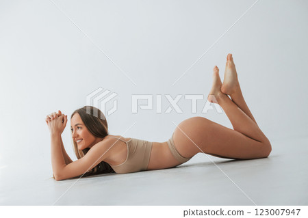Smiling when lying down on the floor. Woman in underwear with slim body type is posing in the studio Smiling when lying down on the floor. Woman in underwear with slim body type is posing in the studio 123007947