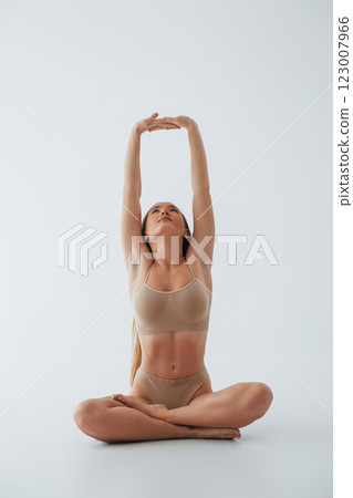 Doing yoga exercises. Woman in underwear with slim body type is posing in the studio 123007966