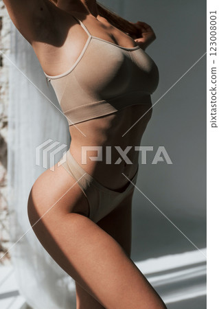 Dark room with sunlight beams. Woman in underwear with slim body type is posing in the studio 123008001