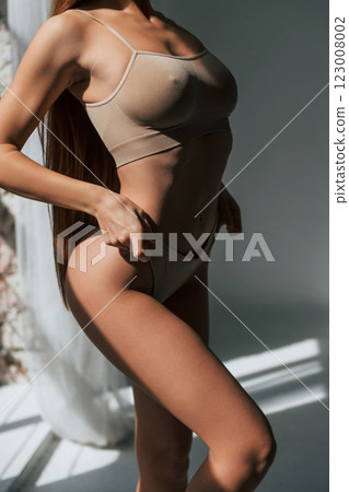 Dark room with sunlight beams. Woman in underwear with slim body type is posing in the studio 123008002