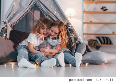 Embracing each other. Two little girls is in the tent in domestic room together Embracing each other. Two little girls is in the tent in domestic room together 123008911