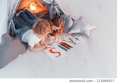 Writing S letter. Conception of learning and education. Two little girls is in the tent in domestic room together 123008917
