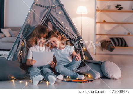 Wondered and holding paper with info or art on it. Two little girls is in the tent in domestic room together 123008922