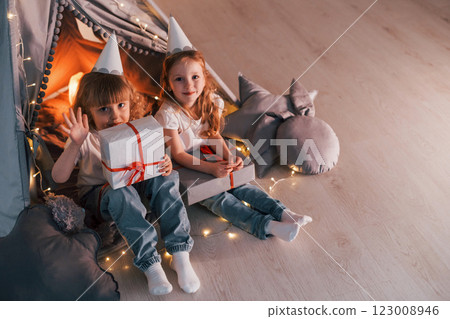 Holding gift boxes. Conception of presents and holidays. Two little girls is in the tent in domestic room together 123008946