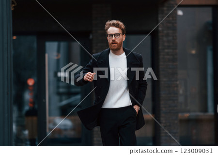 Running out of time. Stylish man with beard and in glasses is outdoors near building 123009031