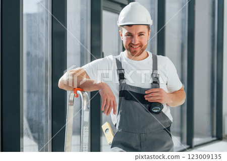 Smiling and posing. Repairman is working indoors in the modern room Smiling and posing. Repairman is working indoors in the modern room 123009135