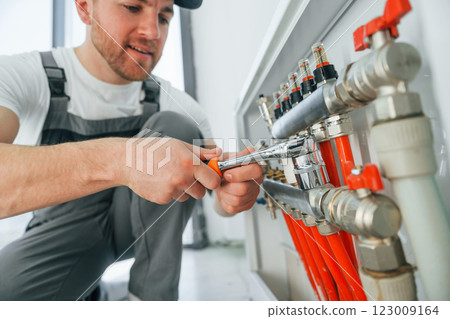 Working with pipes. Repairman is working indoors in the modern room Working with pipes. Repairman is working indoors in the modern room 123009164