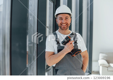 Using drill by installing windows. Repairman is working indoors in the modern room Using drill by installing windows. Repairman is working indoors in the modern room 123009196