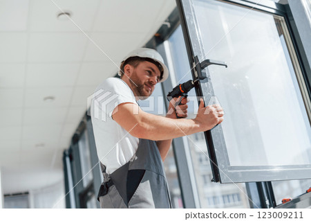 In grey uniform. Repairman is working indoors in the modern room 123009211