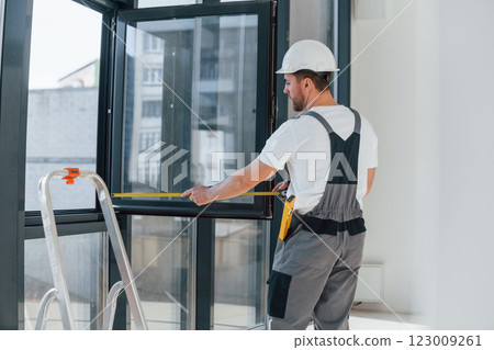 Using measure tape. Repairman is working indoors in the modern room 123009261