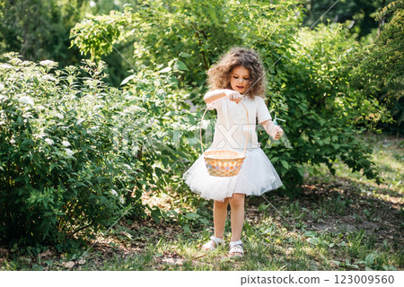 Easter egg hunt. Girl child Wearing Bunny Ears Running To Pick Up Egg In Garden. Easter tradition. Baby with basket full of colorful eggs. 123009560