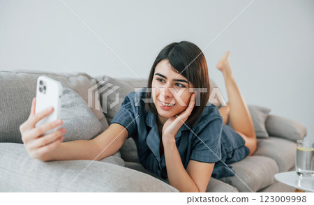 With phone. Laying down on the sofa. Young woman is at home. Conception of beauty With phone. Laying down on the sofa. Young woman is at home. Conception of beauty 123009998