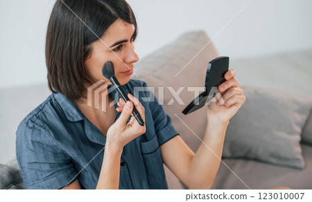 Holding brush and doing face make up. Young woman is at home. Conception of beauty 123010007