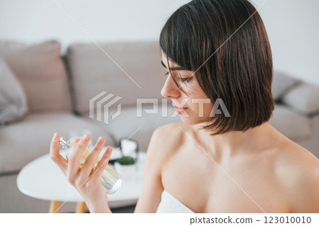 Holding glass with parfume. Young woman is at home. Conception of beauty Holding glass with parfume. Young woman is at home. Conception of beauty 123010010