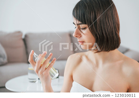 Holding glass with parfume. Young woman is at home. Conception of beauty Holding glass with parfume. Young woman is at home. Conception of beauty 123010011