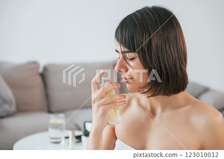 Holding glass with parfume. Young woman is at home. Conception of beauty Holding glass with parfume. Young woman is at home. Conception of beauty 123010012