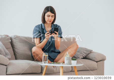 Sitting on the sofa and doing make up. Young woman is at home. Conception of beauty 123010039