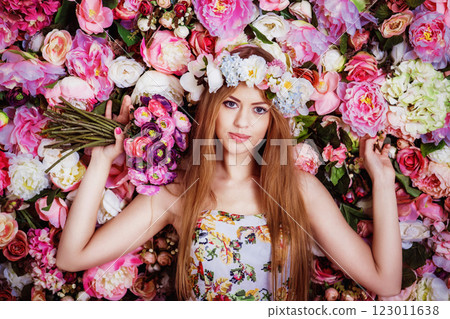 A beautiful young girl with flowers bouquet near a floral wall. 123011638