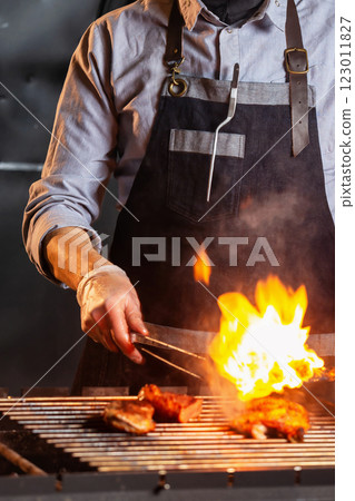 Chief cook is preparing meat at open fire grill at kitchen background. Vertical image. 123011827